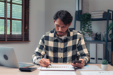 Businessman use smartphone and taking notes on paper while checking financial and accounting report