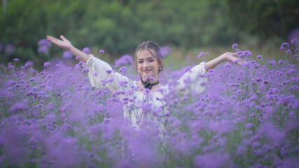 A pretty young Asian girl in a white dress among the beautiful verbena flowers blooming in the field. Portrait fashion natural garden.