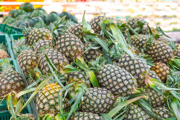 Shelf with fresh whole pineapples at grocery market. Exotic fruits from organic farms. Merchandising fruit in market buyers.