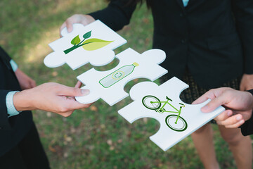 Business people or corporate partnership joining ECO friendly idea puzzle of jigsaw together as...