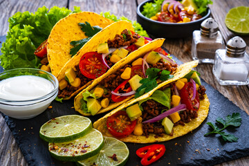 Tacos with ground beef, avocado, corn and fresh vegetables on wooden table 
