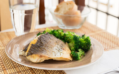 Fried fillet of sea bass with garnish of broccoli on black warm stone plate