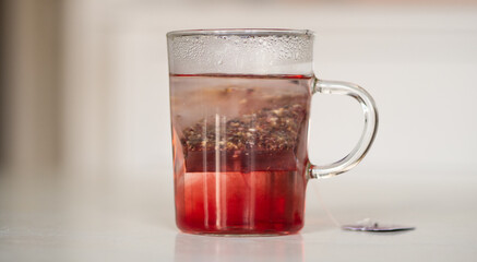 Tisane au cassis qui infuse dans une tasse transparente sur une table blanche