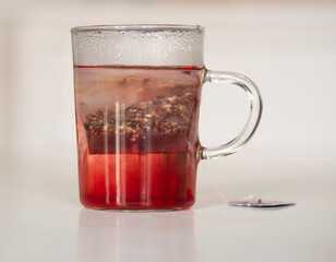 Tisane au cassis qui infuse dans une tasse transparente sur une table blanche