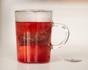 Tisane au cassis qui infuse dans une tasse transparente sur une table blanche