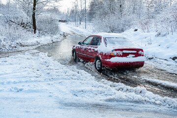 The car rides on a road with melted snow and ruts from the wheels in the spring