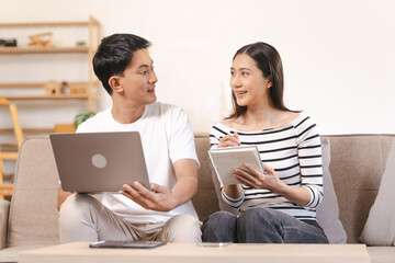 Fototapeta premium young Asian couple engaged in online shopping, wife woman holds notepad note list while husband man compares choices on smartphone. and call for price and discount, promotion.