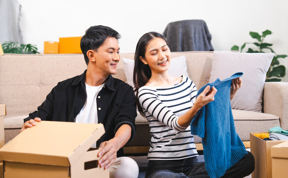 happy Asian couple unpacking boxes and sharing a moment with a blue sweater, suggesting they are moving into a new home together.
