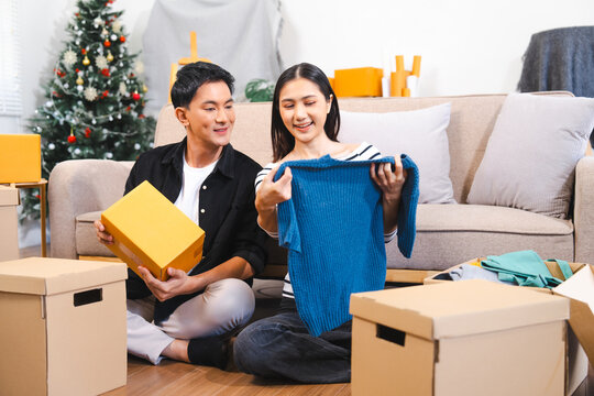 happy Asian couple unpacking boxes and sharing a moment with a blue sweater, suggesting they are moving into a new home together.