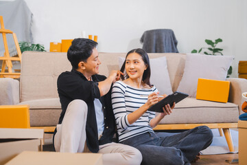 Excited Asian couple celebrates a win, sitting among moving boxes in a living room with a Christmas tree.