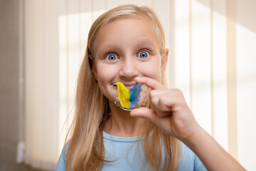 Dental Plate Retainer in Little Girl Hands. Blue and Yellow Removable Aligning Orthodontic Braces in Child.