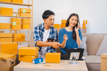 Asian people SME business woman and man couple joyfully showcasing products during a live stream in a room filled with packing boxes.