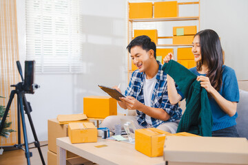 Asian people couple man and woman happily displaying products to smartphone camera for live stream in living room with boxes, home office.