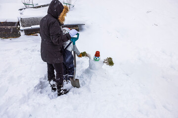 View of woman and child joyfully sculpting  small snowman together in their backyard. Sweden.