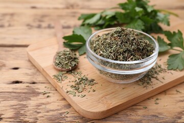 Bowl and spoon with dried parsley on wooden table, closeup. Space for text