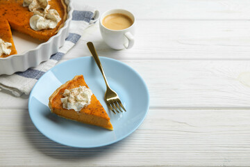 Delicious pumpkin pie with whipped cream, fork and cup of coffee on white wooden table. Space for text