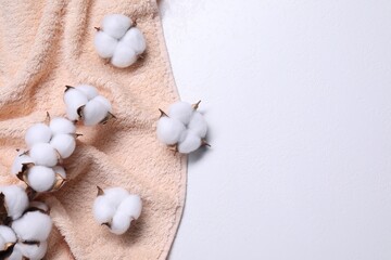 Fototapeta na wymiar Cotton branch with fluffy flowers and beige terry towel on white background, top view. Space for text