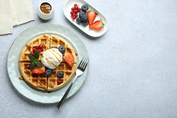 Delicious Belgian waffles with ice cream, berries and caramel sauce served on grey table, flat lay....