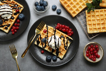 Delicious Belgian waffles with ice cream, berries and chocolate sauce on grey table, flat lay