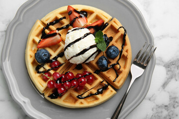 Delicious Belgian waffles with ice cream, berries and chocolate sauce on light marble table, top...