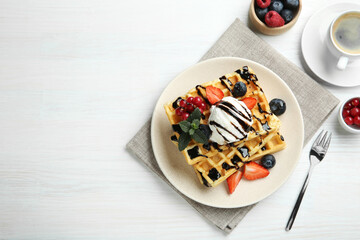 Fototapeta na wymiar Delicious Belgian waffles with ice cream, berries and chocolate sauce served on white wooden table, flat lay. Space for text