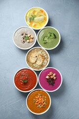 Tasty broth and different cream soups in bowls on gray table, flat lay