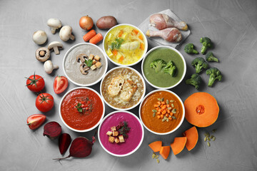 Tasty broth, different cream soups in bowls and ingredients on gray table, flat lay