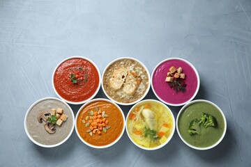 Tasty broth and different cream soups in bowls on gray table, flat lay