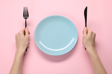 Woman with fork, knife and empty plate at pink table, top view - Powered by Adobe