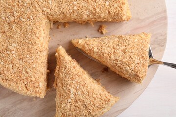 Taking piece of delicious Napoleon cake from table, top view