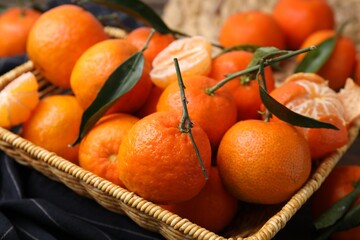 Fresh ripe tangerines with green leaves in wicker basket on table, closeup