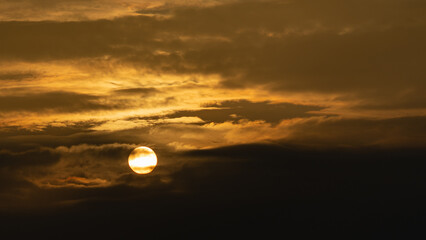 Dramatic winter sunset in monochrome gold with the sun's disk partially hidden behind majestic swirling clouds