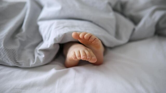 Little child's feet in bed covered with blanket