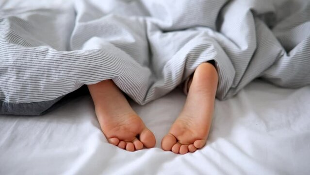 Little child's feet in bed covered with blanket