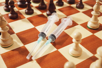 Medical syringes and chess pieces on a chessboard close up