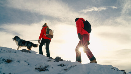Active couple hiking on extreme terrain in the snowy mountains with their dog in winter