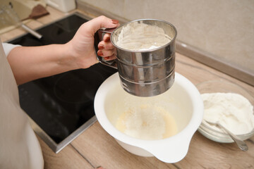 Female hands pour flour into a bowl for cake in the kitchen, sifts flour.
