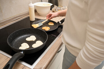 Woman cooking heart shaped pancakes in a frying pan in the kitchen.