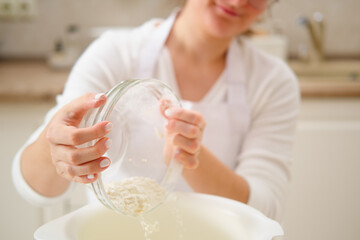 Closeup on woman sifting flour in a glass bowl at home. Process of cooking pecan pie in home...
