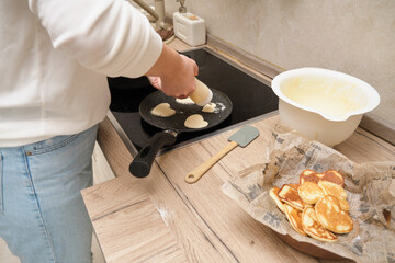 Female hands making pancakes in a frying pan on the stove in the kitchen