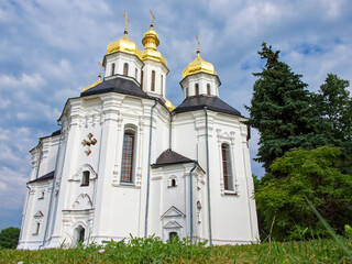 Fototapeta na wymiar The Orthodox Church of St. Catherine, a resplendent white church with gilded domes and crosses, as it stands in perfect harmony with the surrounding lush greenery and the tranquil blue sky.