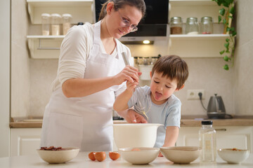 Mother and baby boy in the kitchen at home. Happy family preparing food. Process of cooking pecan...