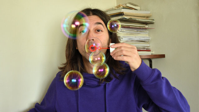ragazzo con capelli lunghi soffia bolle di sapone colorate dentro casa