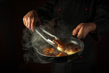 Frying delicious pancakes for dinner. Hot frying pan in the hand of the cook and tongs. Black space for menu or recipe © Виталий Борковский
