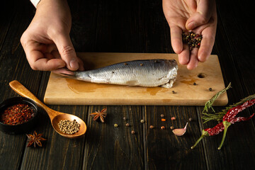 Cooking marinated Atlantic herring fish with aromatic spices by the hands of a chef on a cutting...