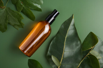 Body spray in amber glass cosmetic bottle, loofah, eucalyptus leaves on green background. SPA natural organic beauty product packaging design, branding. Beauty salon banner mockup. Flat lay, top view. - obrazy, fototapety, plakaty