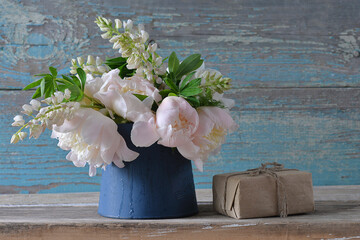 Bouquet of white peonies and lupines in blue jug and hand made gift box on the old blue paint...