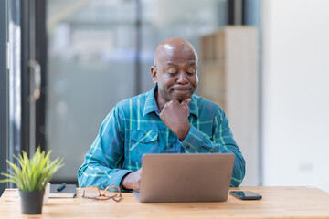 serious American professional business man, wearing glasses working on laptop, remote studying using computer looking at screen watching seminar webinar at home office.