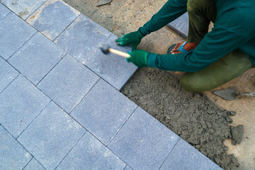 A tiler is laying cement block slabs in front of a newly built house.