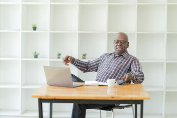 Portrait of happy African American small business owner. Millennial black smiling, sitting and using the laptop, and holding a cup of coffee work in modern office.